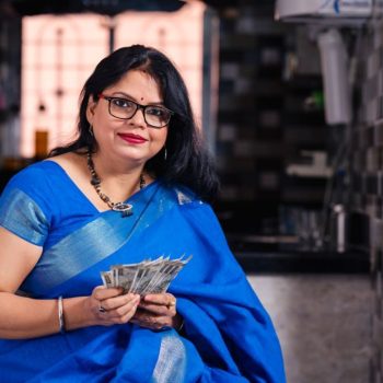 Young Indian woman holding currency notes while sitting on sofa at home.